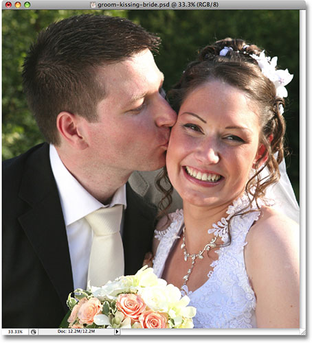 A wedding photo of a groom kissing the smiling bride. 