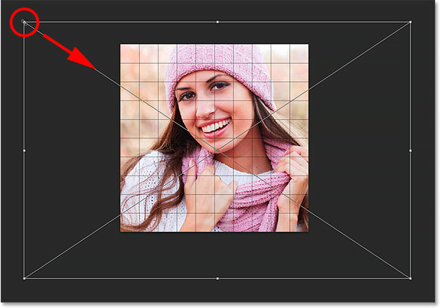 Dragging a corner handle to resize the image inside the grid. Image © 2014 Photoshop Essentials.com.